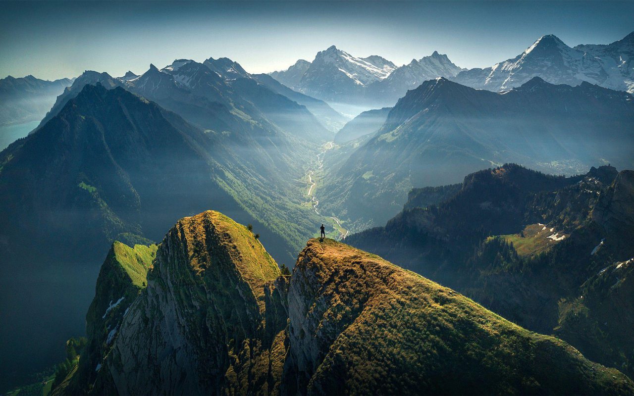 Vue panoramique sur les Alpes suisses avec un randonneur au sommet d’une montagne, illustrant la beauté des paysages suisses et les zones reculées accessibles à Internet via Starlink